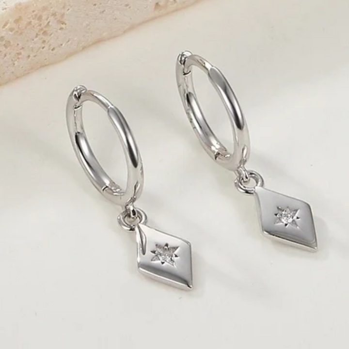 White gold plated diamond drop earrings featuring small hoops with dangling rhombus-shaped charms, each with a central sparkling crystal resembling a North Star. These elegant earrings are available in Ottawa, Ontario, Canada.