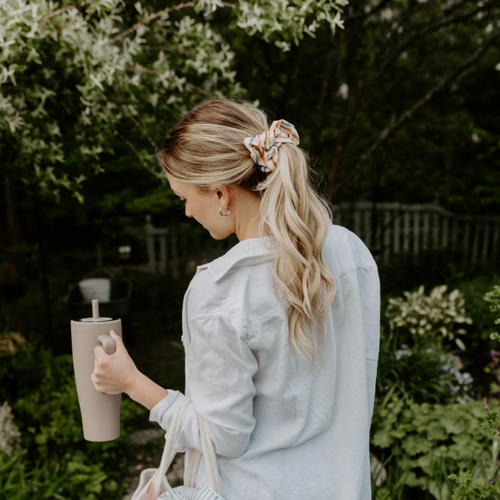 Sundeck Stripes Petite Scunchie, a fluffy hair tie in a creamy white with a rainbow of stripes in a blonde woman's hair.