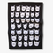 A black tea towel with a pattern of white cat faces. The cat faces are arranged in a grid-like pattern and vary in size and shape.