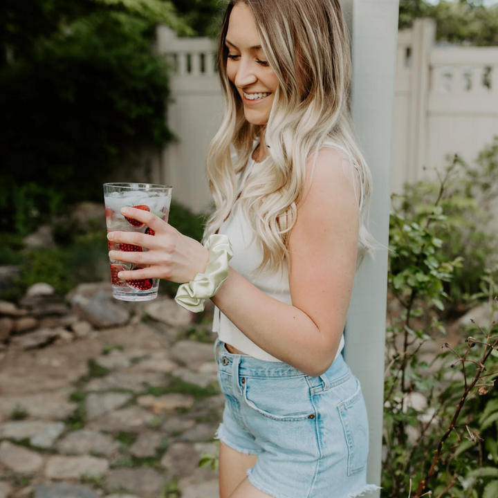 Chili Lime Satin Petite Scunchie, a fluffy satin scrunchie in a pastel green colour on a blonde woman's wrist holding a glass of water.
