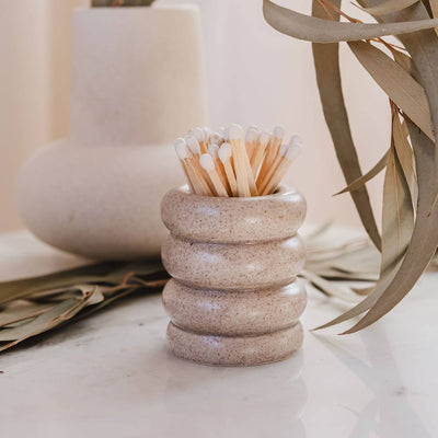 Decorative stone holder with matches on a surface with plants in the background