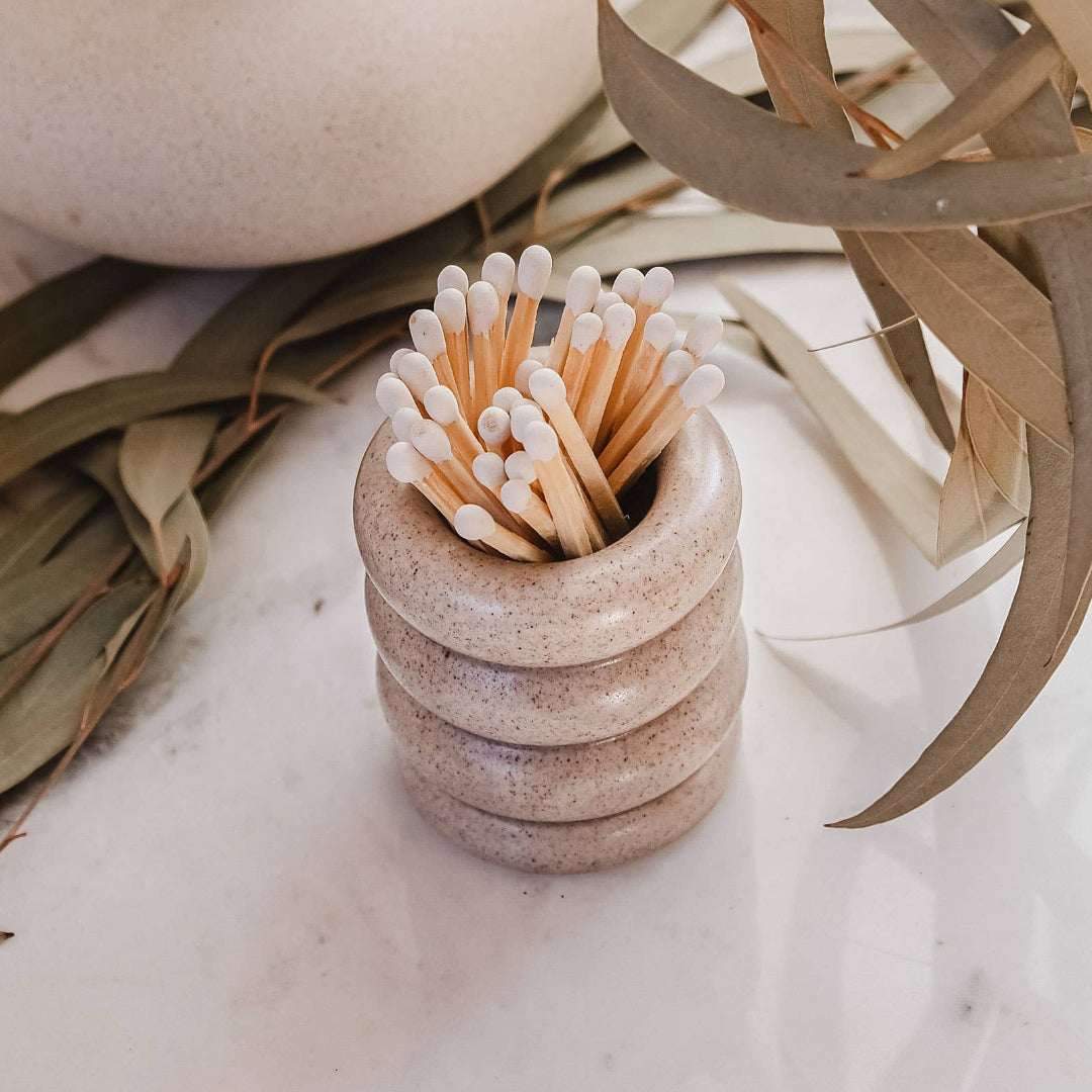 Stack of ceramic cups with wooden matches on a marble surface with dried plants.