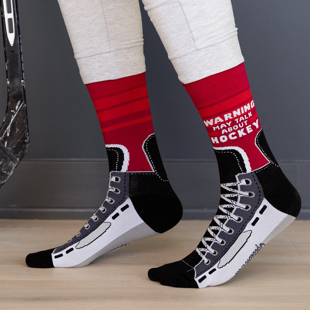 Person wearing red and black socks with text, standing on a wooden floor.