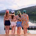 Four friends standing on a dock by a lake with mountains in the background
