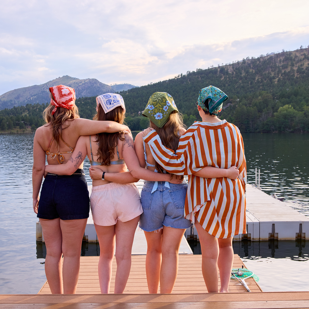 Four friends standing on a dock by a lake with mountains in the background