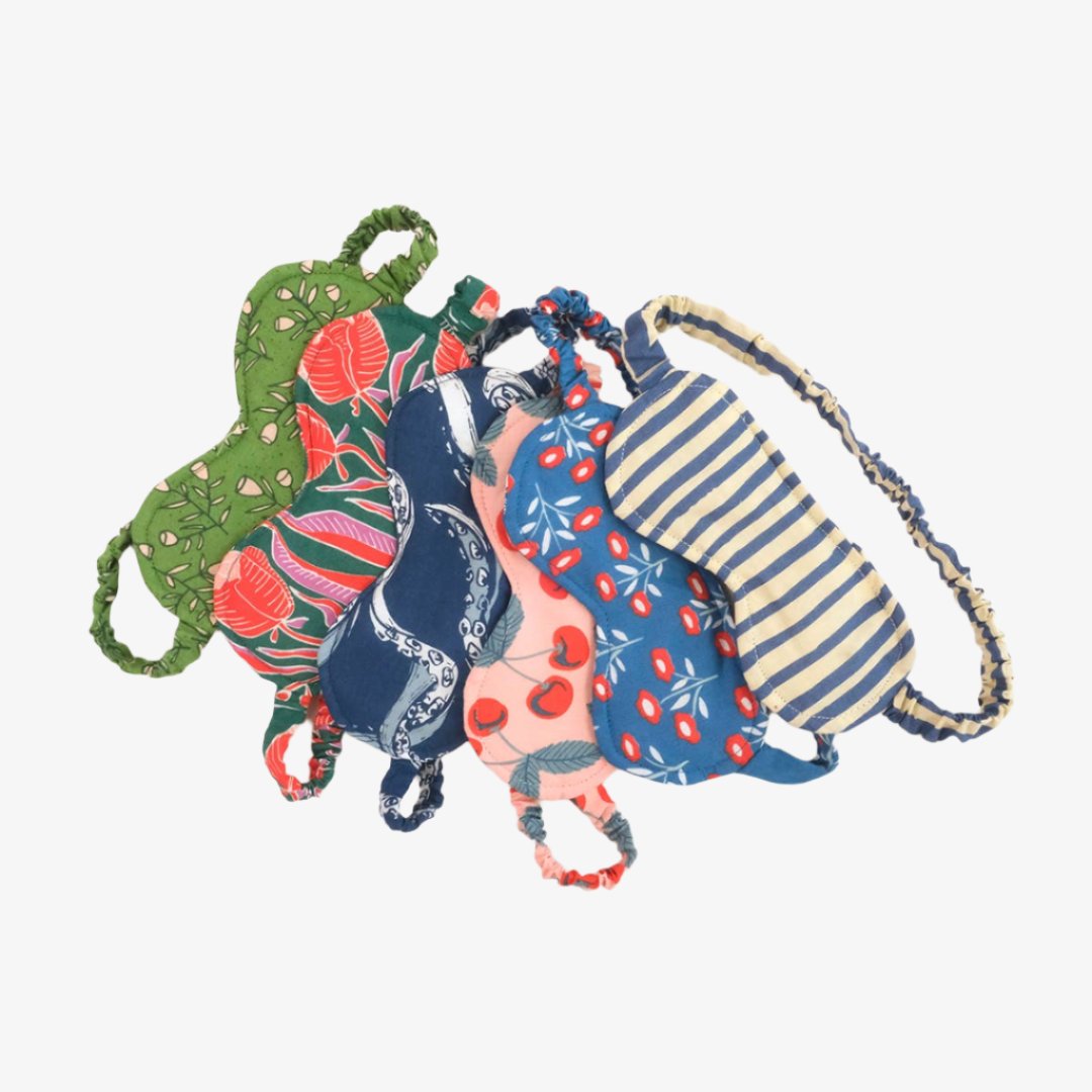 A collection of five sleep masks in various patterns. The masks are made of colorful fabric and have elastic bands to fit around the head. The patterns include cherries, flowers, stripes, and an abstract design.