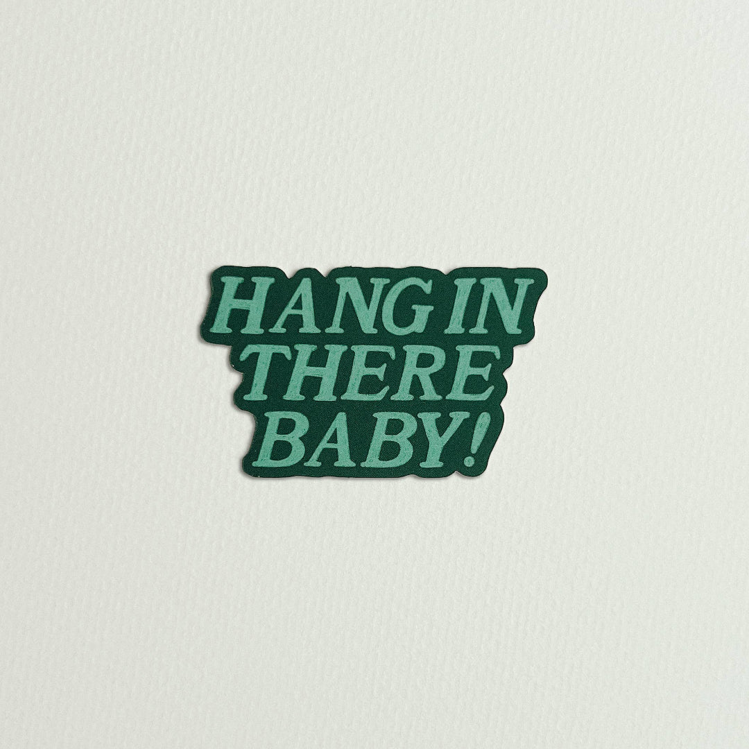 Green sticker with 'HANG IN THERE BABY!' text on a light gray background