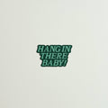 Green sticker with 'HANG IN THERE BABY!' text on a light gray background