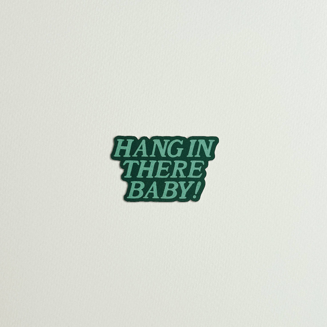 Green sticker with 'HANG IN THERE BABY!' text on a light gray background