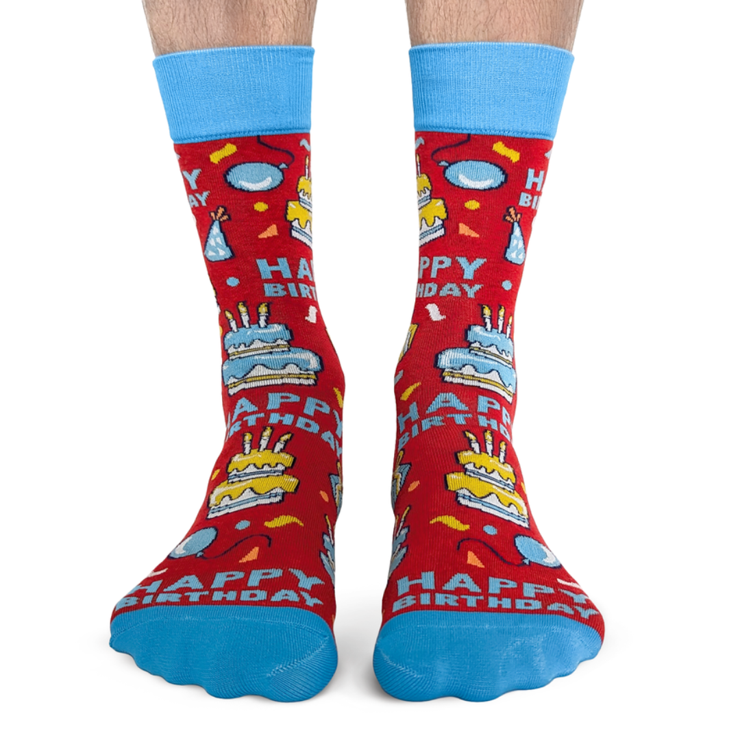 Red socks with 'Happy Birthday' and cake designs, worn by a person on a white background