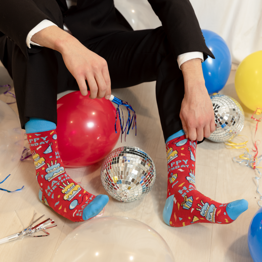 Person in a suit with colorful socks sitting on the floor with balloons and disco balls.
