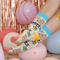 Person wearing colorful socks with cartoon designs in a festive setting with balloons and rose gold streamers.