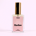 A bottle of Charleston & Harlow perfume named "Harlow." The bottle is clear glass with a gold cap. The label is pink with the brand name and perfume name in a bold, playful font. The fragrance notes are listed as "Peach, Moscato, Pineapple."