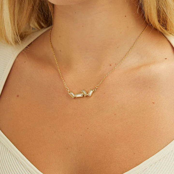 A gold necklace with several rectangular-shaped crystals on a pink card with the brand name 