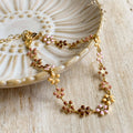 A gold chain bracelet with a row of colorful enamel flower charms. The flowers are in shades of pink, orange, and yellow.