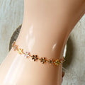 A gold chain bracelet with a row of colorful enamel flower charms. The flowers are in shades of pink, orange, and yellow.