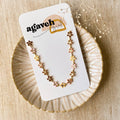 A gold chain bracelet with a row of colorful enamel flower charms. The flowers are in shades of pink, orange, and yellow.