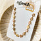 A gold chain bracelet with a row of colorful enamel flower charms. The flowers are in shades of pink, orange, and yellow.