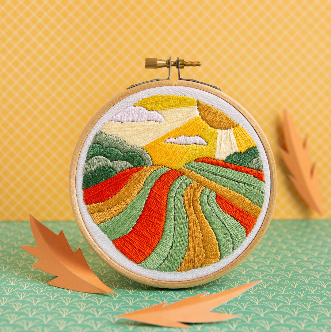 Embroidery hoop with a colorful landscape design on a yellow background