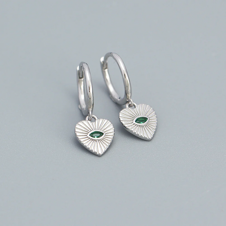 Silver mini hoop earrings featuring dangling heart charms, each with a central marquise-cut green crystal and radiating etched lines. These dainty and elegant earrings are available in Ottawa, Ontario, Canada.