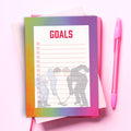 A pastel gradient notepad with the word 'GOALS' in red at the top and a hockey-themed illustration on the cover, styled on a pink background with a pink pen beside it.