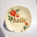 Decorative plate with red roses and the word 'hello' on a white background