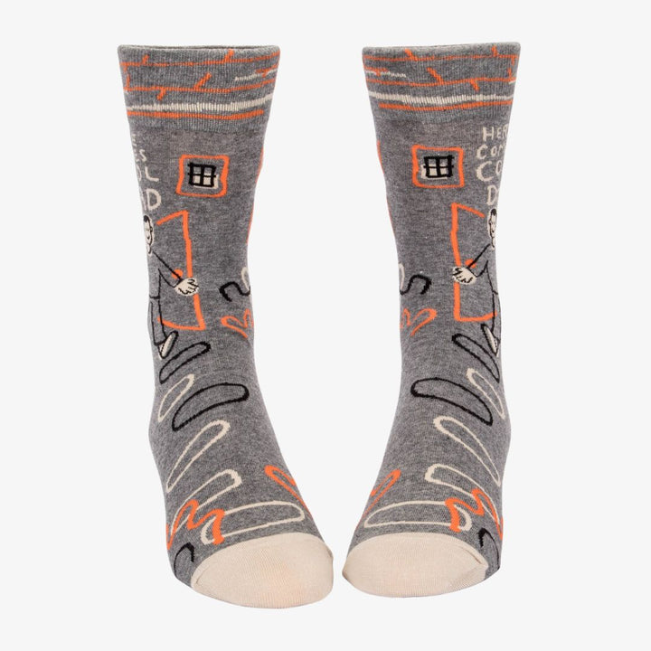 A pair of grey men's crew socks with orange, white, and black abstract lines. One sock features a cartoon drawing of a man with an orange background and the text 