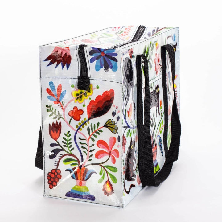 A rectangular shoulder tote bag with black handles, featuring a whimsical pattern of black cats, colourful flowers, and foliage against a white background.