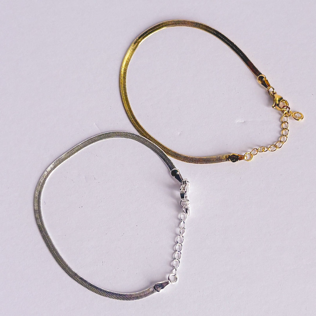 Two bracelets, one gold and one silver, on a light gray background