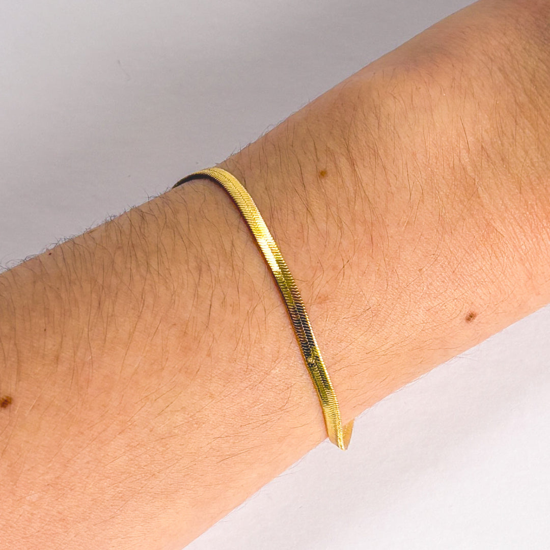 Gold bracelet on a wrist with a neutral background