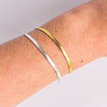 Two bracelets, one silver and one gold, on a wrist against a light gray background.