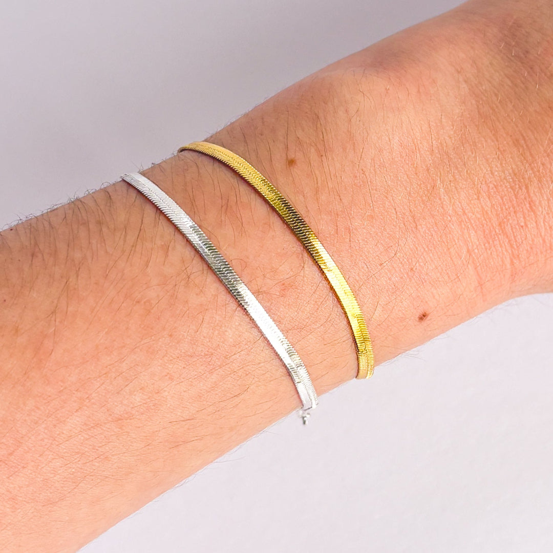 Two bracelets, one silver and one gold, on a wrist against a light gray background.