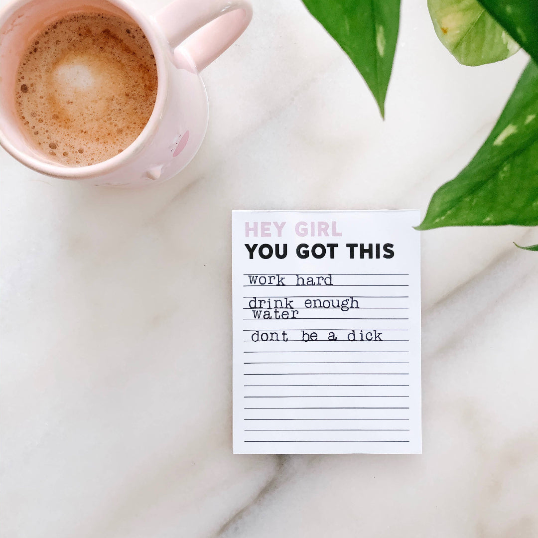 Notepad with motivational quote next to a pink mug on a marble surface