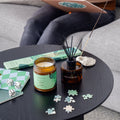 Candle, diffuser, and puzzle pieces on a table with a person sitting in the background.