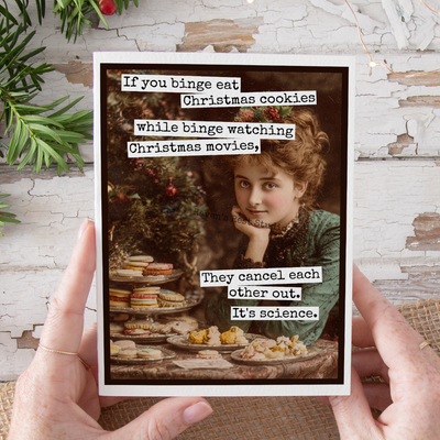 Person holding a card with a vintage-style illustration of a woman and text about Christmas cookies and movies.