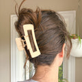 Person with a beige hair clip in their hair, standing in front of a mirror.