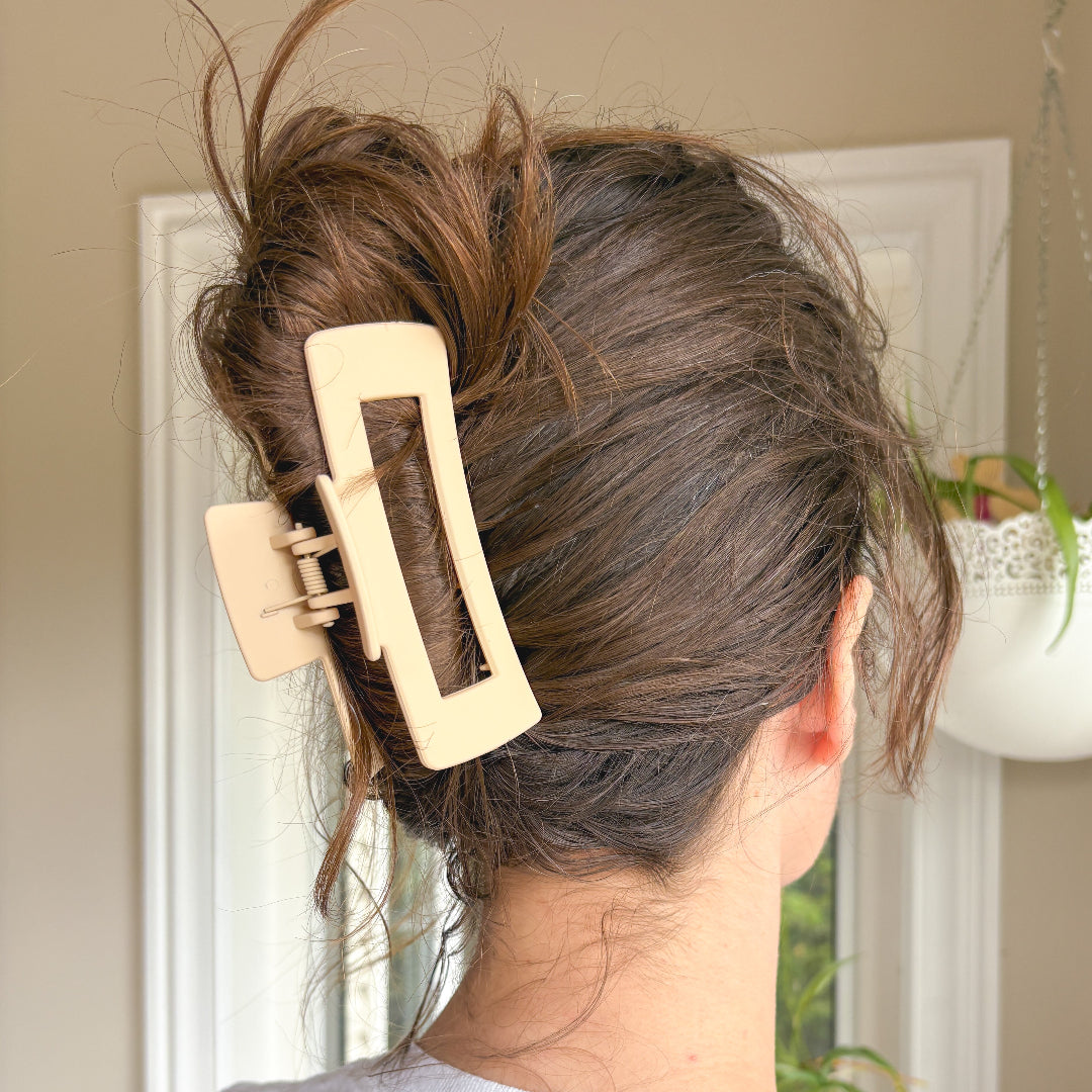 Person with a beige hair clip in their hair, standing in front of a mirror.