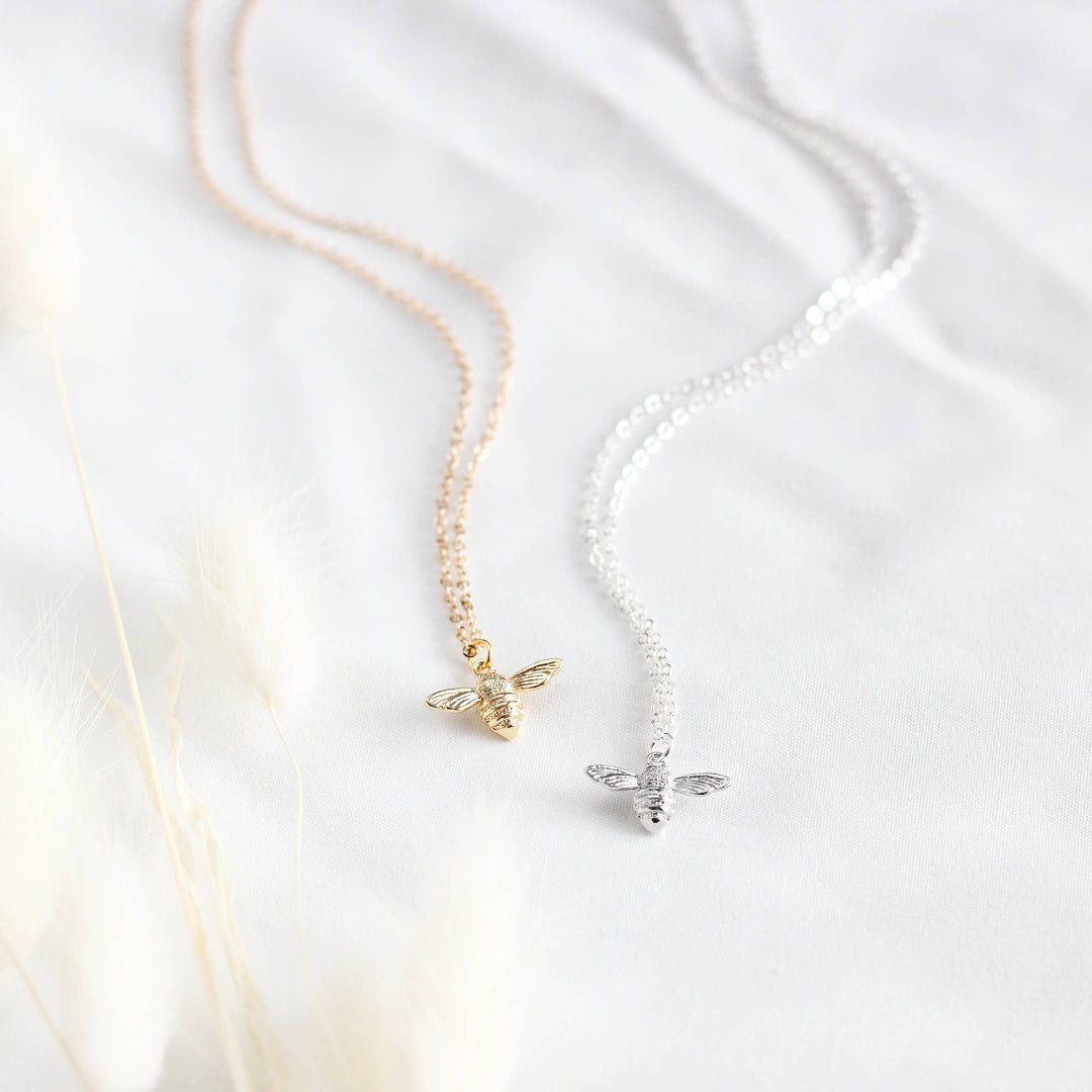 Two bee-shaped pendants on gold and silver necklaces against a white background