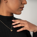 Person wearing a gold necklace with a bee pendant, touching their neck.