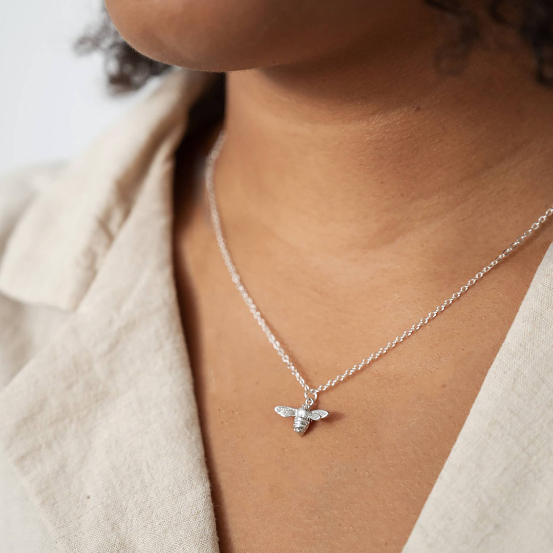 Silver bee necklace on a person wearing a beige jacket.