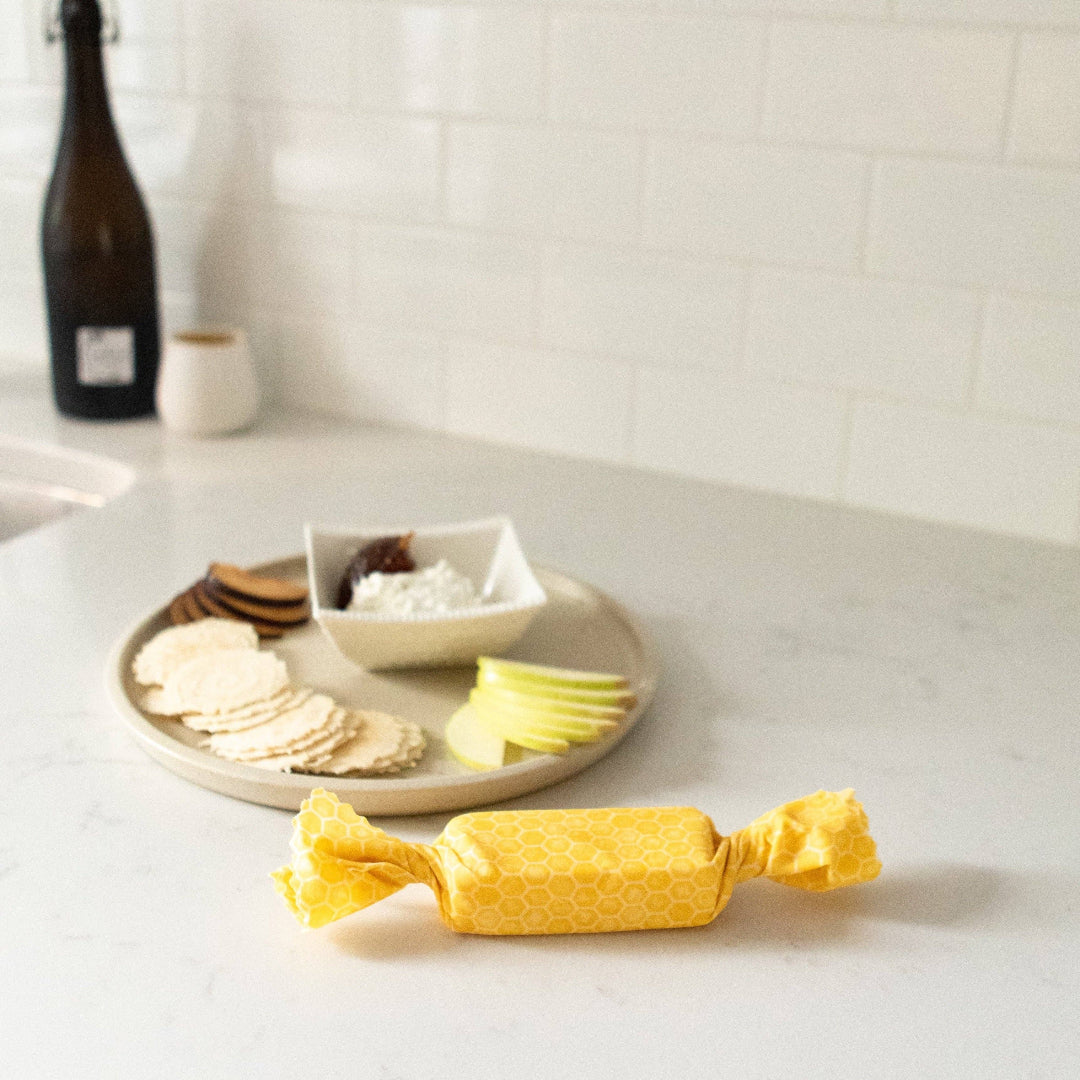 Yellow wrapped product on a kitchen counter with a plate of snacks in the background.