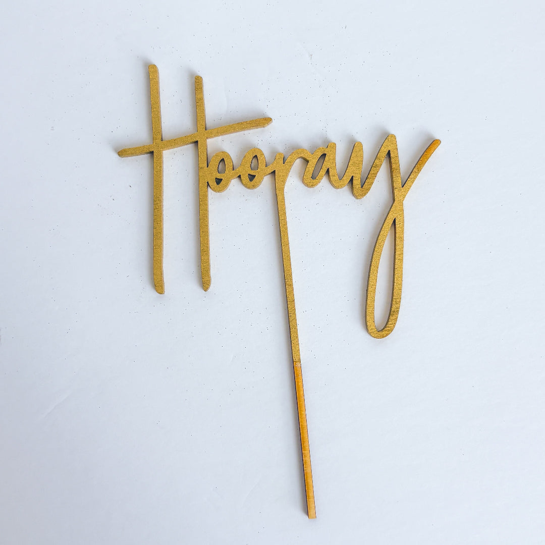 Gold 'Hoopla!' cake topper on a white background