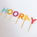 Colorful 'HOORAY' letter cake toppers on sticks against a white background