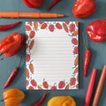Notepad with chili pepper design surrounded by real red and yellow peppers on a blue background