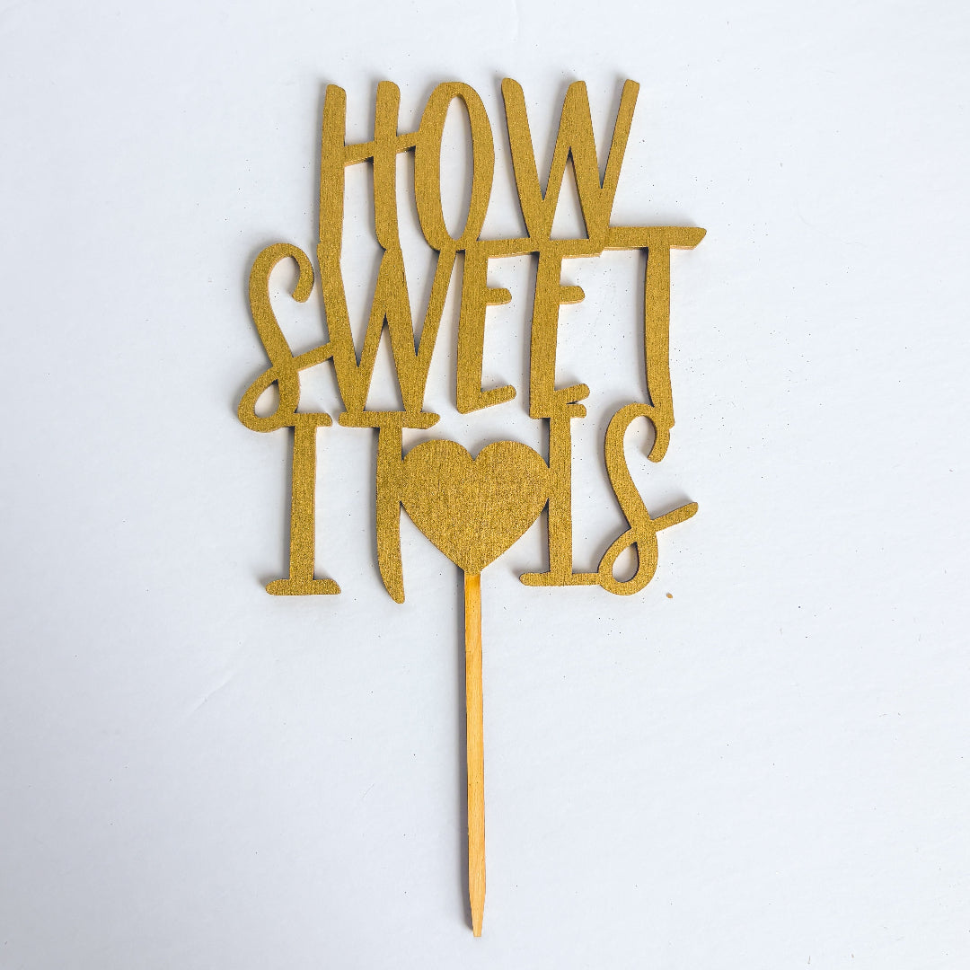 Gold cake topper with 'How Sweet It Is' text on a white background
