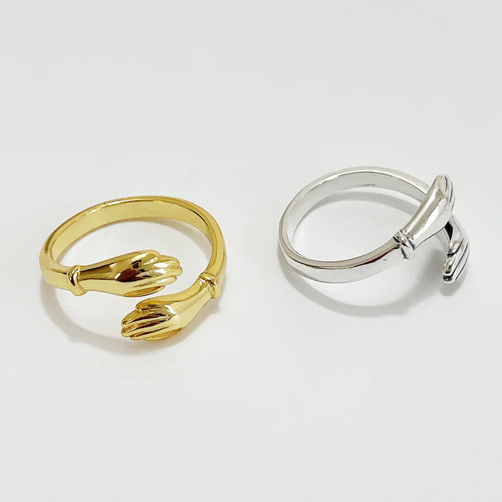 A set of gold and silver hug rings, each featuring two hands gently wrapping around the finger, symbolizing love, friendship, and support. These open band rings are available in Ottawa, Ontario, Canada.