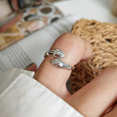 A sterling silver hug ring, featuring two hands gently wrapping around the finger, symbolizing love, friendship, and support. This open band ring is available in Ottawa, Ontario, Canada.