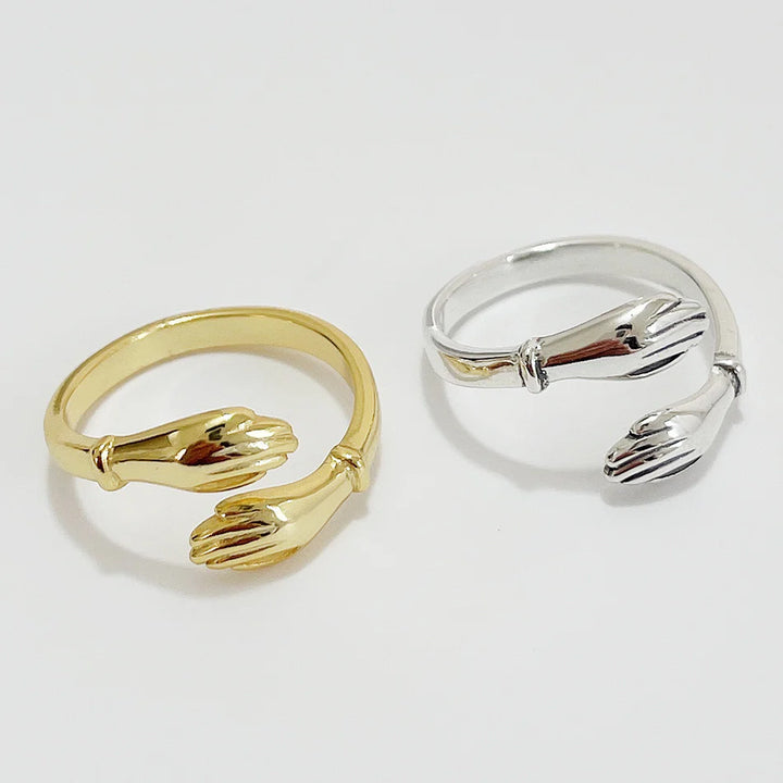 A set of gold and silver hug rings, each featuring two hands gently wrapping around the finger, symbolizing love, friendship, and support. These open band rings are available in Ottawa, Ontario, Canada.
