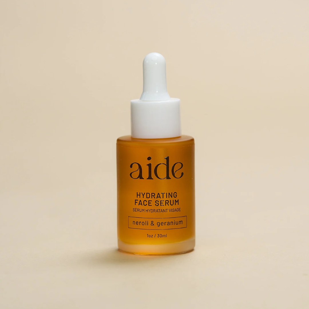 Aide Bodycare Hydrating Face Serum, featuring a small glass bottle with a dropper and a label with 'aide' logo, 'Hydrating Face Serum', and 'neroli & geranium' text, displayed on a light-colored surface. The serum is natural and available in Ottawa, Ontario, Canada.