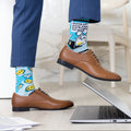 Person wearing blue socks with colorful designs and brown shoes, sitting on a laptop.